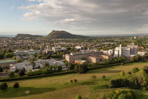 Aerial photo with the University of Edinburgh King's Buildings science campus in the foreground, looking towards the hills of Arthur's Seat and Salisbury Crags and the sea in the distance.